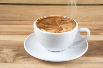Hot cappuccino or latte art coffee. A cup of coffee on the wooden table with roasted beans. Morning breakfast with coffee. Hearts shape created by pouring steamed milk.