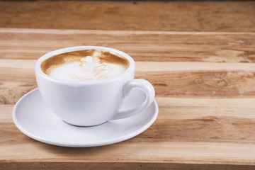 Hot cappuccino or latte art coffee. A cup of coffee on the wooden table with roasted beans. Morning breakfast with coffee. Hearts shape created by pouring steamed milk.