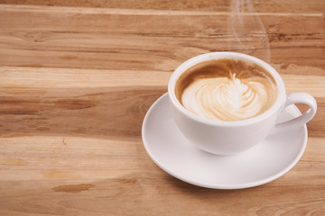 Cappuccino or latte art coffee. Free hand pouring some foam of milk on top. A white ceramic cup on the wood table with some coffee beans. The best food and drink in the world. Fresh energy everyday.