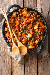 Delicious Picadillo cooked from ground beef with vegetables, raisins and spices close-up in a frying pan. Vertical top view