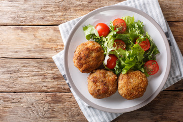 Tasty Danish pork minced meat patties in breading with fresh vegetable salad close-up on the table. horizontal top view