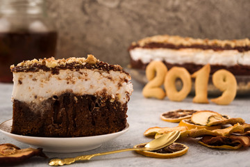 Nice cake. Piece of chocolate cake. Festive dessert on a plate. Figures 2019. Dry fruit slices. A teaspoon of metal. Light background.