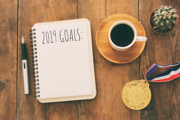 Top view 2019 goals list with notebook, cup of coffee over wooden desk.