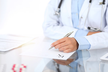 Doctor woman filling up prescription form while sitting at the desk in hospital close-up. ...