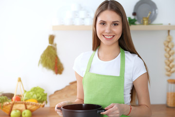 Obraz na płótnie Canvas Young happy woman cooking soup in the kitchen. Healthy meal, lifestyle and culinary concept. Smiling student girl preparing vegetarian meal at home