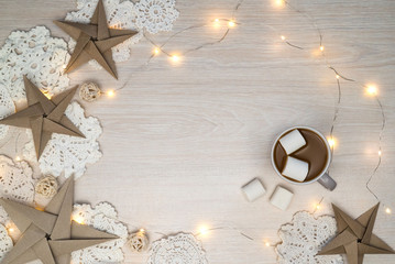 Cosy Christmas composition with lights, coffee, marshmellows, paper stars, chrochet doilies on...