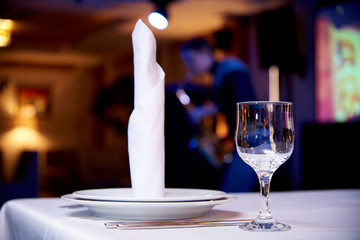 Empty glass on a served table on a blurred background a musician playing the saxophone in a cozy restaurant.