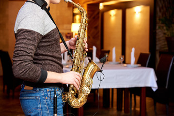 The musician plays the saxophone in the evening in a cozy restaurant.