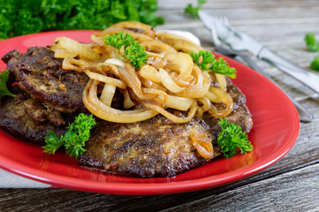 Juicy slices of fried liver and onions on a red plate.