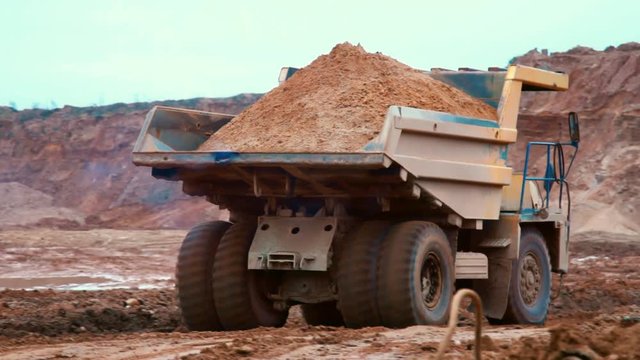 Dirty tipper truck transports sand on road in quarry. Large yellow dumper truck