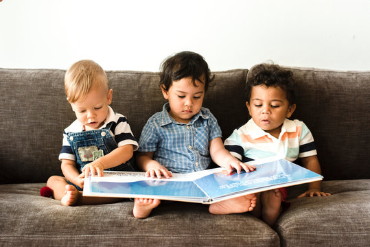 Three little boys reading a book on a sofa