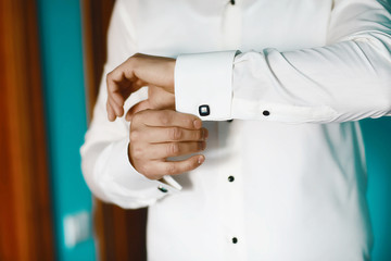 Grooms morning preparation, handsome groom getting dressed and preparing for the wedding, the bridegroom wears cufflinks in a white shirt