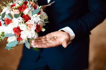 gold wedding rings in the bride's hand in a suit with a bouquet of flowers of white and red color