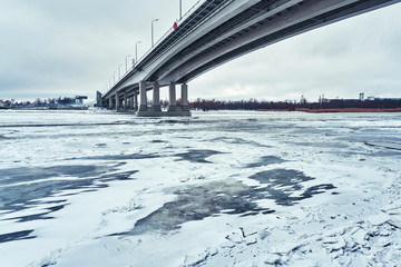 A new gray bridge over a frozen river with ice connects the two banks of the big city
