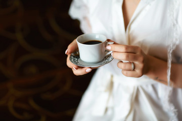 A bride's morning, coffee for breakfast, transparent white peignoir and gentle hands. A picture of an elegant female hand with fine manicure pulling to a perfect cup of coffee