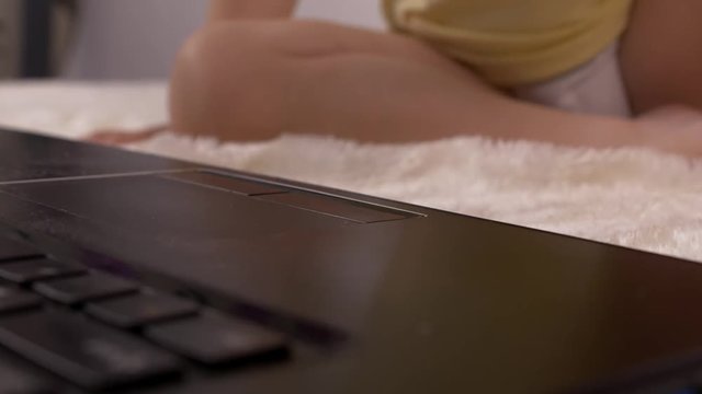 A small child presses a finger on the button on the laptop keyboard, close-up, baby and computer, education