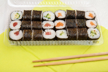 Sushi rolls in nori seaweed in plastic box with wooden sticks.