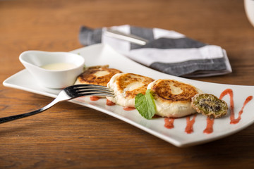 Cottage cheese pancakes with sour cream on white plate on wooden background