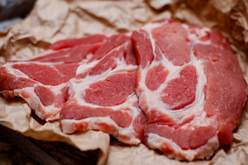Sliced fresh raw meat on cooking paper on wooden table background. Chop pork neck. 