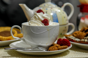 Coffee with cream and cakes on table. Big mug of coffee, sweet cakes and old ewer in modern surrounding of living room.