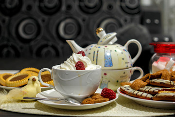Coffee with cream and cakes on table. Big mug of coffee, sweet cakes and old ewer in modern surrounding of living room.