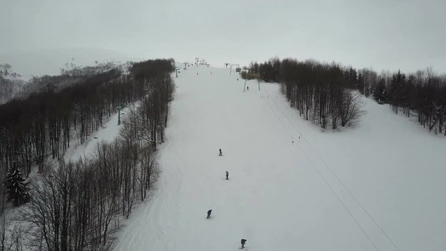 Flight over people using ski lift in mountains. Aerial view of ski resort.