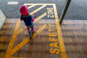 Young girl in pink outfit and pink helmet riding a kick-scooter waiting on a platform at train station in safety zone
