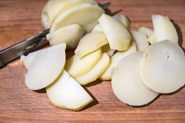 sliced raw potatoes and a knife on a wooden chopping Board