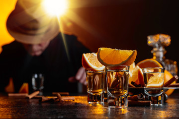 Glasses of tequila with orange and cinnamon sticks on a table in bar.
