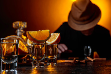 Glasses of tequila with orange and cinnamon sticks on a table in bar.