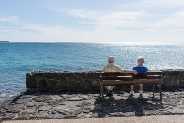 Elderly couple looks at the sea and sitting on a bench. Travel in old age