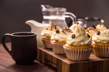 Tiramisu cupcakes decorated with cocoa powder and coffee grains on a wooden board next to jugs of...