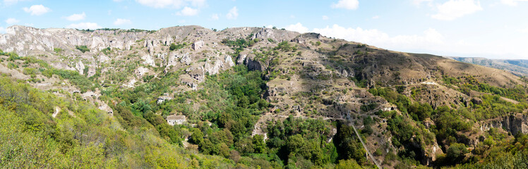 Fototapeta na wymiar Panorama beautiful canyon at Khndzoresk cave settlement (13th-century, used to be inhabited till the 1950s) with a suspension bridge underneath, Syunik region, Armenia