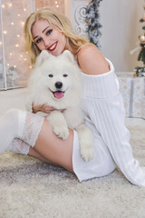 beautiful blonde in white clothes with a white husky on the background of the fireplace