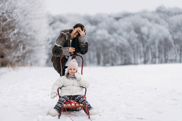 Little sisters have fun in the winter on the snow. Girls ride a sled in a park in the nature. riding on snow slides in winter time. little sisters have fun in the winter on the snow