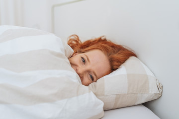 Laughing young woman cuddling under the duvet