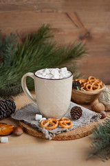 A cup of hot latte with marshmallows and some salty pretzels on wooden table. Christmas time, winter season.