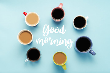A lot of multi-colored cups of coffee and coffee drinks on a blue background with the text Good morning. Circle shape. Concept breakfast with coffee, coffee with friends. Flat lay, top view