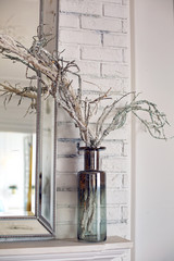 large transparent bottle stands by the mirror with a branch of silver dust glitter decor for new year and Christmas