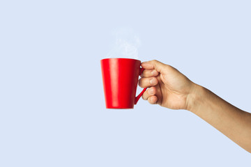Female hand holding a red cup with hot coffee on a blue background. Side view