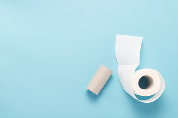 A roll of unwrapped toilet paper and an empty toilet paper roll against a blue background. Flat lay, top view