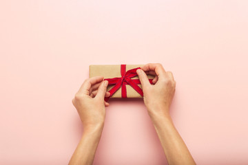 Female hands holding a gift box on a pink background with a question mark. Surprise concept, waiting for a gift for the holidays, birthday, christmas, wedding. Flat lay, top view