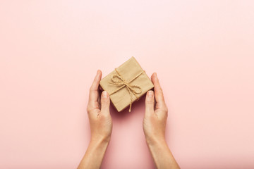 Female hands holding a gift box on a pink background with a question mark. Surprise concept, waiting for a gift for the holidays, birthday, christmas, wedding. Flat lay, top view