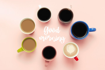 A lot of multi-colored cups of coffee and coffee drinks on a pink background with the text Good morning. Circle shape. Concept breakfast with coffee, coffee with friends. Flat lay, top view