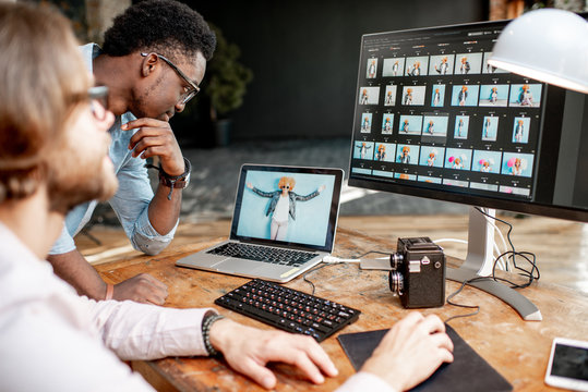 Two male photographers choosing woman's portraits at the working place with two computers in the studio