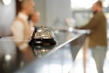 Fotobehang Moderne luxe Hotel Receptie Balie met bel. Service Bell lokaliseren bij de receptie. Silver Call Bell op tafel, receptionisten en klant op de achtergrond. In het hotel. Concept. © skvalval