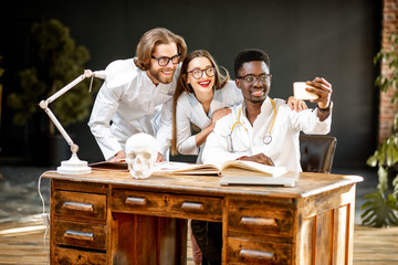 Group of a young multi ethnicity physicians or medical students in uniform making selfie photo while studying indoors
