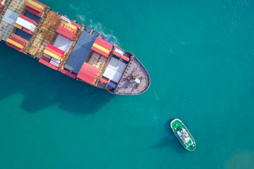 Large container ship pulled into port by tugboats - Top down aerial image