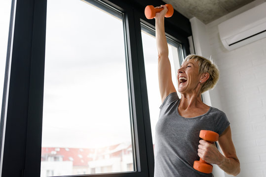 Active good looking elderly woman smiling and holding dumbbells while working out indoors