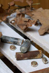 Spent batteries, coated with corrosion. Different shapes and sizes. They lie on a wooden box among the dead autumn leaves. Environmental protection, recycling.